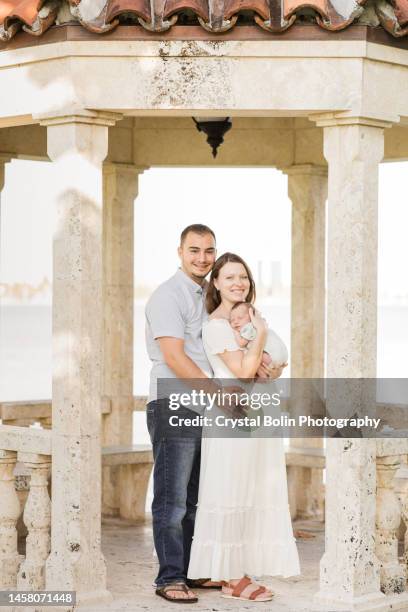 a sweet young family of three snuggled together in a gazebo on the water in a relaxing meditation garden in palm beach, florida for lifestyle newborn family photos - rock baby sleep stock pictures, royalty-free photos & images