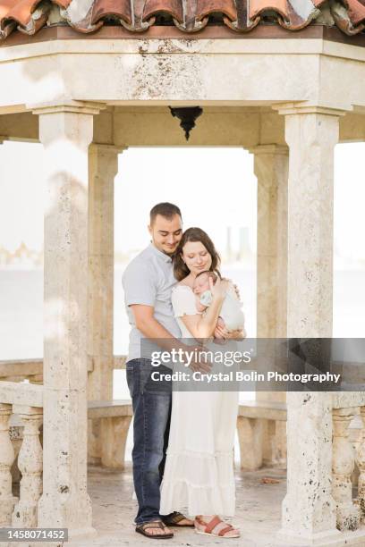 a sweet young family of three snuggled together in a gazebo on the water in a relaxing meditation garden in palm beach, florida for lifestyle newborn family photos - rock baby sleep stock pictures, royalty-free photos & images