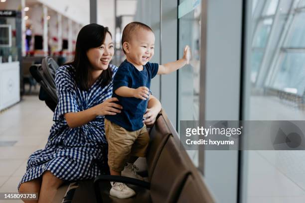 mother and baby looking out window for airplane at airport - airport sitting family stock pictures, royalty-free photos & images