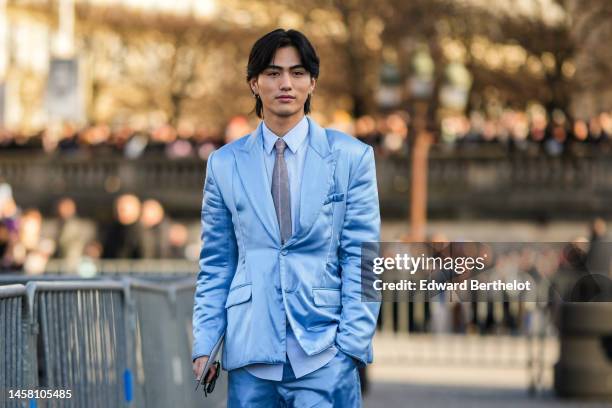 Shuzo Ohira wears silver earrings, a white shirt from Dior, a pale gray tie, a pale blue blazer jacket, matching pale blue suit pants, gold rings,...