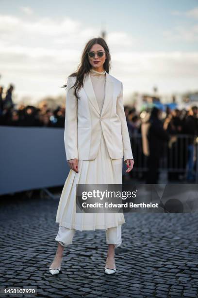 Karlie Kloss wears black sunglasses, gold earrings, a white latte turtleneck pullover, a white latte blazer jacket, a white latte pleated midi skirt,...