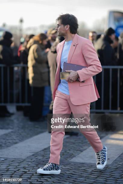 Guest wears sunglasses, a white t-shirt, a pale pink blazer jacket, matching pale pink suit pants, a burgundy shiny leather clutch from Dior, a...