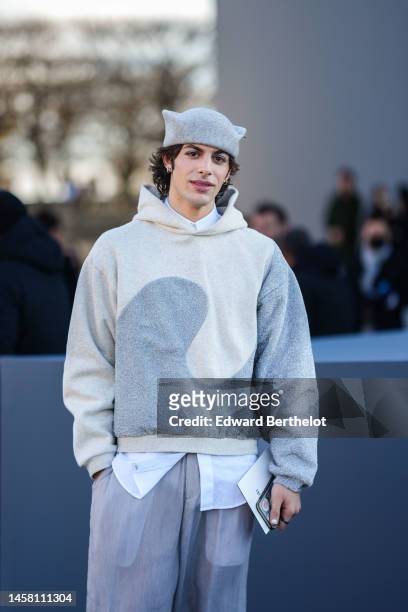Guest wears a pale gray felt wool a hat in the shape of a cat's ear, a white shirt, a white latte with pale gray wavy print pattern hoodie sweater,...