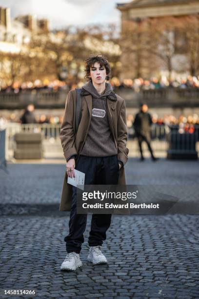 Guest wears a silver pendant earrings, a brown wool hoodie sweater with embroidered logo from Dior, a brown long wool coat, a brown shoulder bag from...