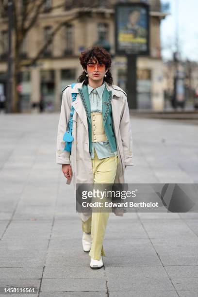 Guest wears orange sunglasses, silver earrings, a blue shiny leather nailed / studded Cagole shoulder bag from Balenciaga, a pale green matte leather...