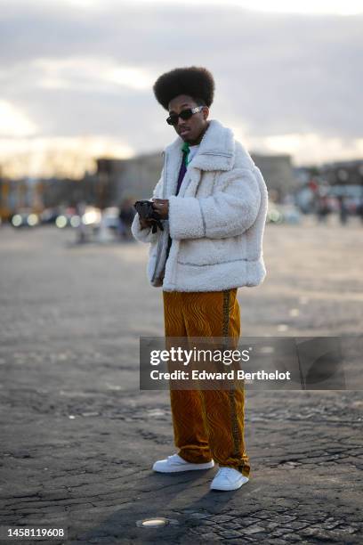 Guest wears black sunglasses from Versace, a purple pullover, a white fluffy zipper oversized coat, a black shiny leather mittens, gold velvet...