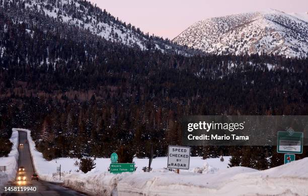 Vehicles drive along a roadway plowed of snow after a series of atmospheric river storms on January 20, 2023 near South Lake Tahoe, California....