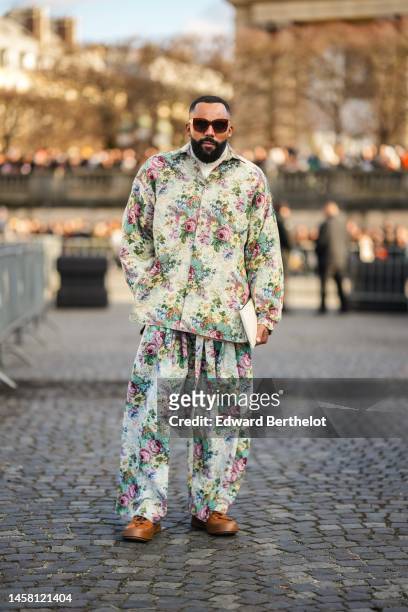 Guest wears red sunglasses, a white latte with embroidered pink / green / yellow flower print pattern oversized zipper jacket, matching white latte...