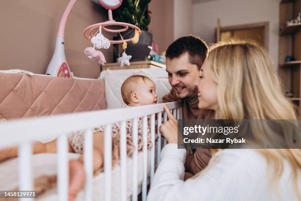 the young cheerful couple enjoying their cute baby in the cradle at home - mother father stock pictures, royalty-free photos & images