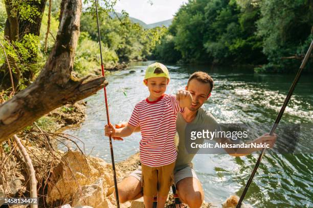 father and son showing their "catch" while fishing - by the river stock pictures, royalty-free photos & images