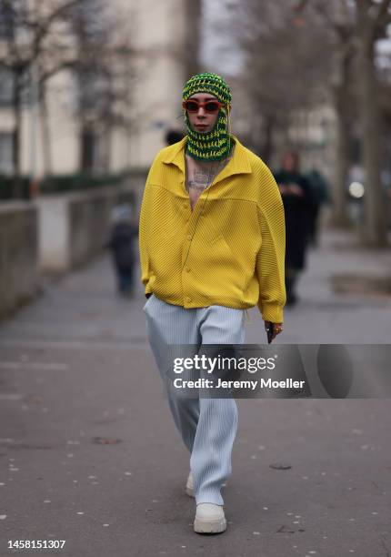 Fashion week guest seen wearing a dark and bright green balaclava, red shades, a yellow oversized jacket, wide blue leg pants and white sneaker...