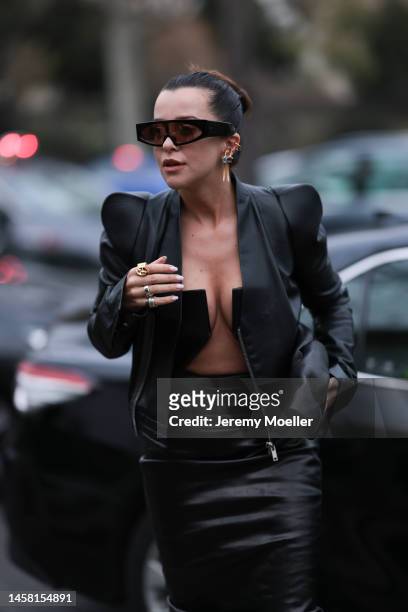 Fashion week guest seen wearing a matching black leather look with a leather jacket and a leather dress with a wide cutout, dark oversized shades and...