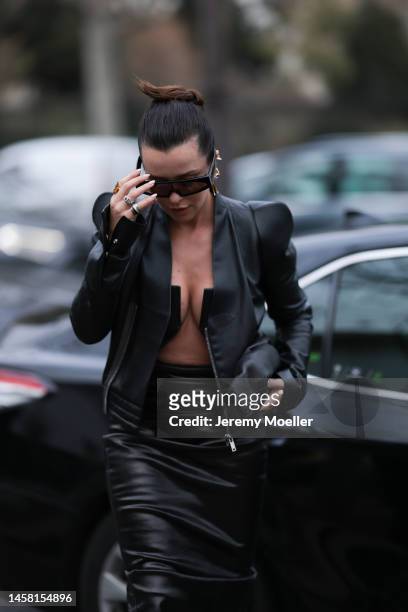 Fashion week guest seen wearing a matching black leather look with a leather jacket and a leather dress with a wide cutout, dark oversized shades and...