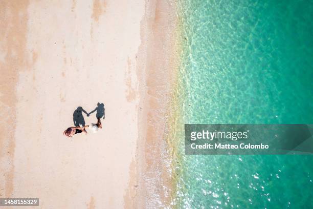 overhead view of couple in swimwear holding hands at the beach - viaggio di nozze foto e immagini stock