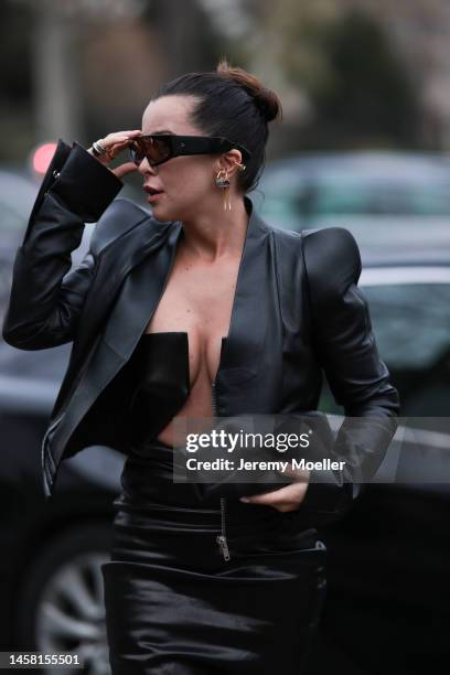 Fashion week guest seen wearing a matching black leather look with a leather jacket and a leather dress with a wide cutout, dark oversized shades and...