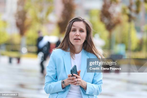 young adult business woman walking at the street and using phone - abrigo azul fotografías e imágenes de stock