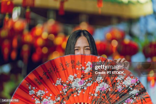 a woman wearing a cheongsam and holding a red fan on chinese new year, there are many red lanterns. - chinese new year red envelope stock-fotos und bilder