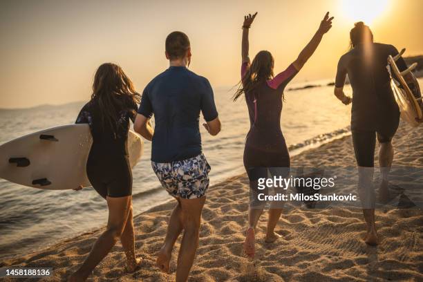 gruppe von freunden surft am strand bei sonnenuntergang - beach hold surfboard stock-fotos und bilder