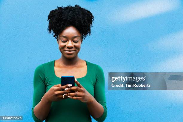 woman using smart phone next to blue wall - digital native stock pictures, royalty-free photos & images