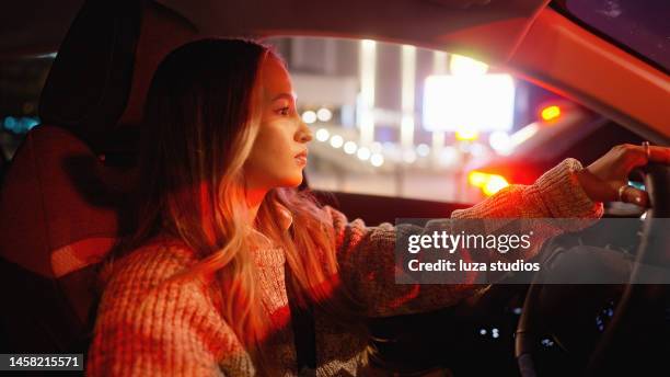 woman driving a car at night, waiting at a red light - traffic light city stockfoto's en -beelden