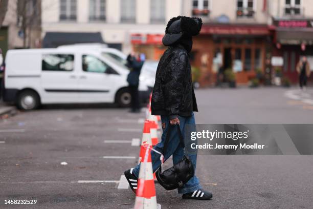 Fashion week guest seen wearing a black fur hat, a black leather jacket, a black bag, black and white sneaker, white shades and blue jeans before the...