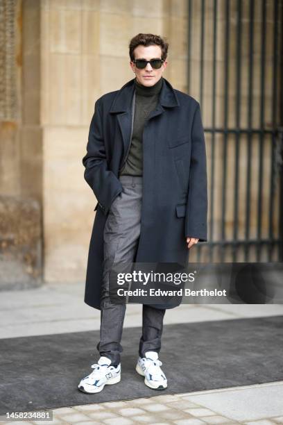 Guest wears black sunglasses, a dark wool turtleneck pullover, a black long coat, gray suit pants, white sneakers from New Balance, outside Louis...