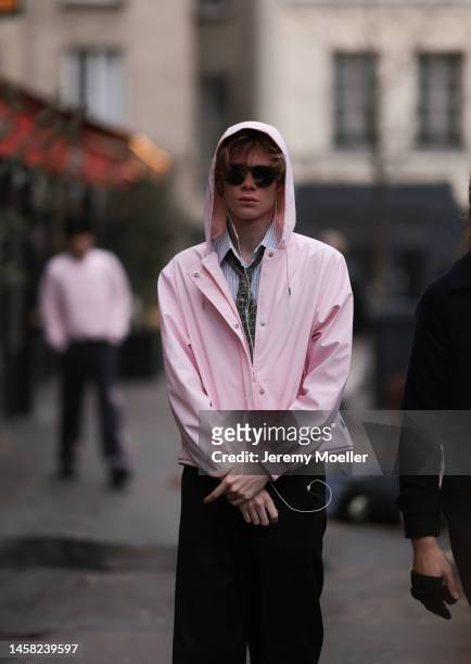 Fashion week guest seen wearing a pink rain jacket, a paisley patterned necktie, a blue and white striped shirt, dark shades and black wide leg pants...