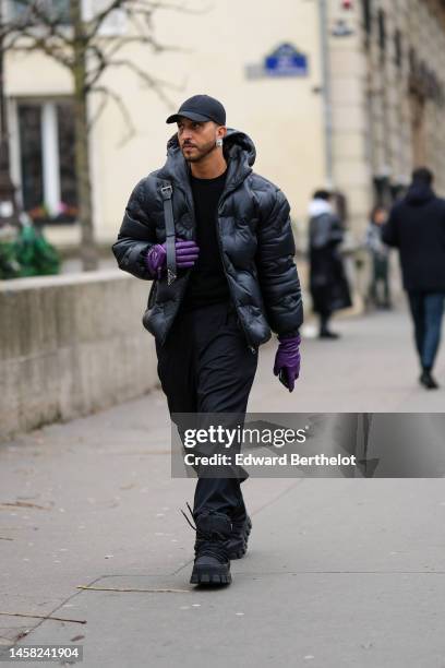Guest wears a black cap, diamonds earrings, a black pullover, a black shiny leather hoodie puffer jacket from Louis Vuitton, dark purple shiny...