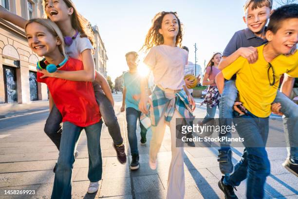 gruppe glücklicher kinder, die auf der straße der stadt laufen - einfaches leben stock-fotos und bilder