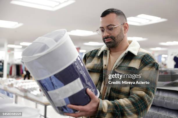 a latinx millennial man with a beard, shops in a department store while wearing eyeglasses and a plaid jacket. - latin american and hispanic shopping bags stockfoto's en -beelden