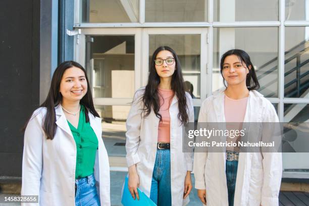 three female medical students wearing medical lab coats and looking at the camera. - medical school building stock pictures, royalty-free photos & images