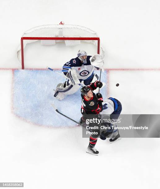 Connor Hellebuyck of the Winnipeg Jets catches the puck out the air as his teammate Neal Pionk battles with Brady Tkachuk of the Ottawa Senators...