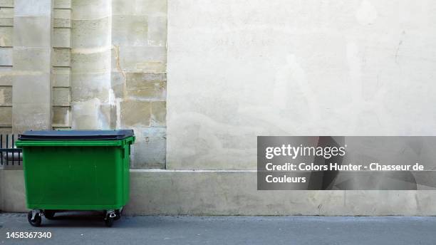 a green bin on a sidewalk and in front of a building in paris - industrial garbage bin fotografías e imágenes de stock