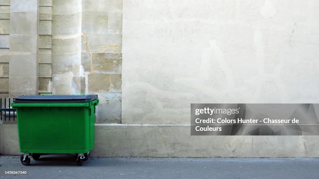 A green bin on a sidewalk and in front of a building in Paris