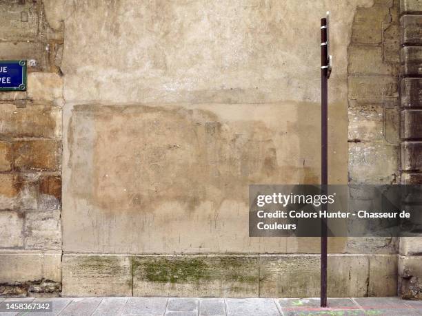 old brown stone and stucco wall, street name sign, cobblestone sidewalk and pole in paris - stone wall stock pictures, royalty-free photos & images