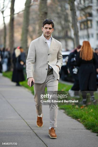 Johannes Huebl wears sunglasses, a white shirt, a beige blazer jacket, matching beige suit pants, camel suede loafers, a khaki wool pullover, outside...