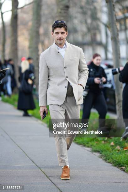 Johannes Huebl wears sunglasses, a white shirt, a beige blazer jacket, matching beige suit pants, camel suede loafers, a khaki wool pullover, outside...