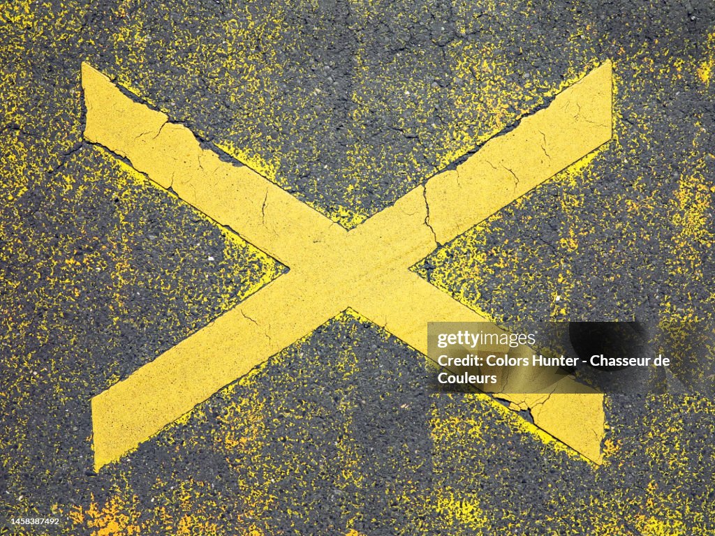 Letter X painted and weathered in yellow on the gray asphalt of a street in Paris