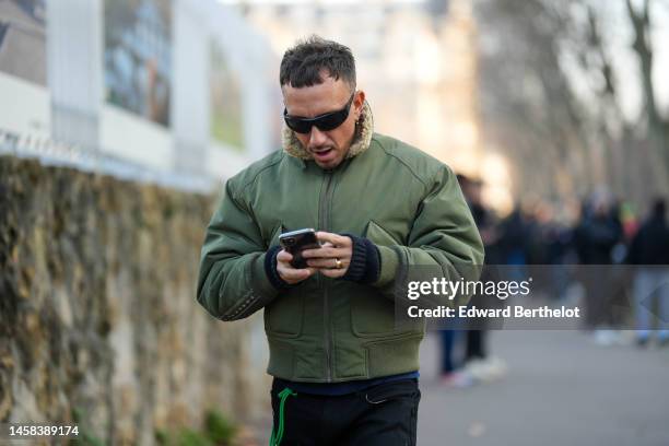 Guest wears black sunglasses, a khaki with fur collar bomber coat, black denim with embroidered shiny leather yoke pants, outside Hermes, during...