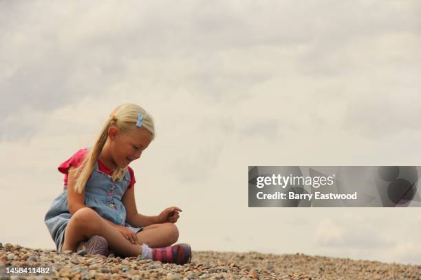 little girl sitting on pebble beach - pinafore dress stock pictures, royalty-free photos & images