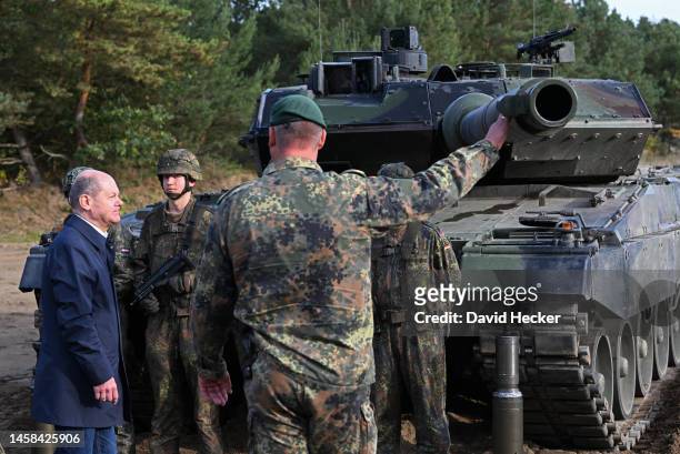 German Chancellor Olaf Scholz chats with troops while standing next to a Leopard 2 main battle tank of the Bundeswehr during a visit to the...
