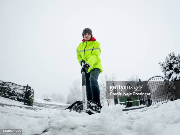 young man shoveling snow from the path in a high vis vest - shoveling driveway stock pictures, royalty-free photos & images