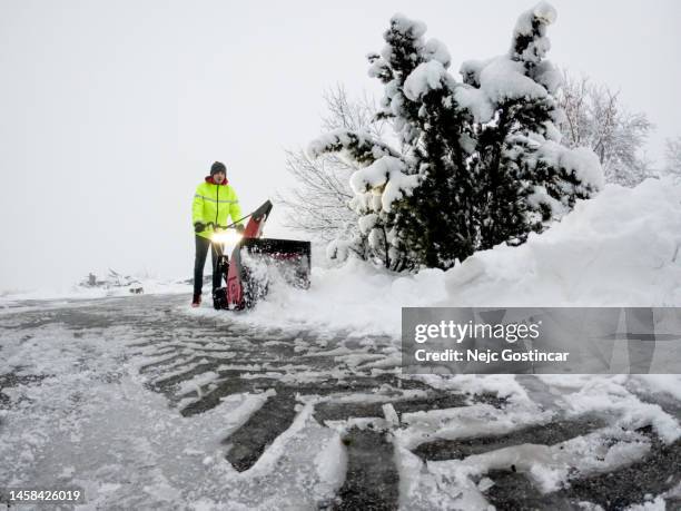 young man clearing snow of a driveway with a red snowblower - sneeuwmachine stockfoto's en -beelden