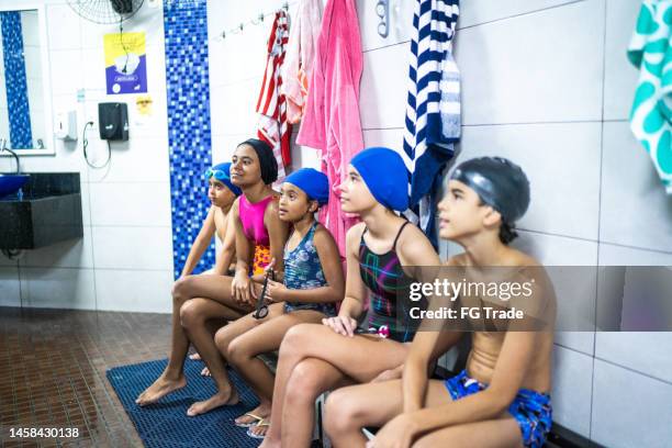 kinder sitzen auf der bank in der umkleidekabine des schwimmvereins - hallenbad stock-fotos und bilder