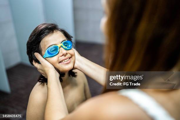 boy getting help to put on swimming goggles in the swimming club locker room - young boys changing in locker room stock pictures, royalty-free photos & images