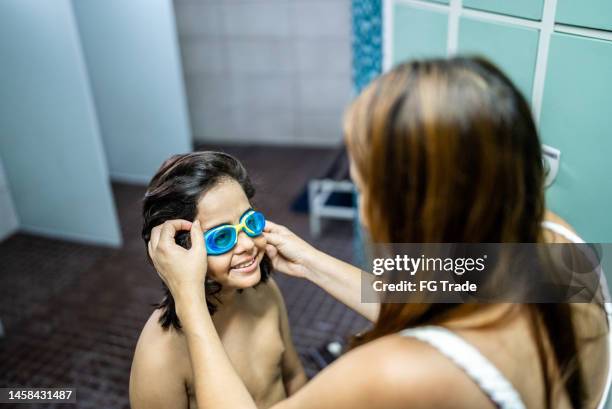 boy getting help to put on swimming goggles in the swimming club locker room - young boys changing in locker room stock pictures, royalty-free photos & images