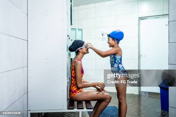 girl helping sister to put on swimming goggles in the locker room - family getting dressed stock pictures, royalty-free photos & images