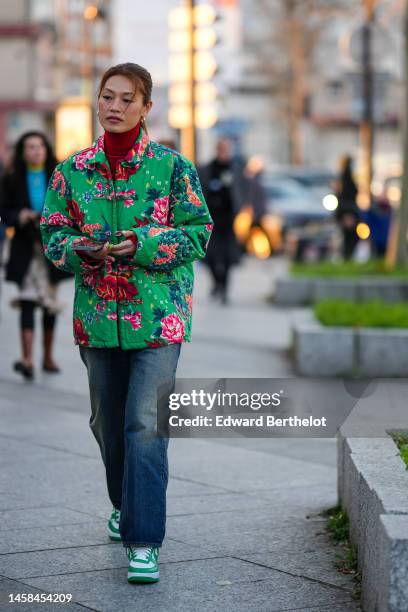 Guest wears a red wool turtleneck pullover, a green with pink and blue flower print pattern jacket, blue faded denim large pants, white and green...