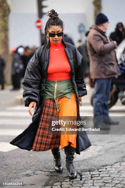 Guest wears black sunglasses, gold earrings, a neon orange turtleneck pullover from Off-White, a black shiny leather quilted long puffer jacket, a...