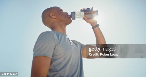 drinking water, fitness and black man after workout, running training and exercise outdoor in sun. blue sky, sport runner and water drink of a athlete with a bottle taking a sports break in nature - bottle water sport stock pictures, royalty-free photos & images